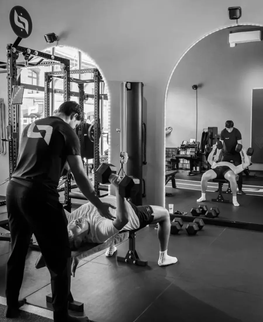 Ein Coach sichert einen Kunden beim Bankdrücken bei VAULT